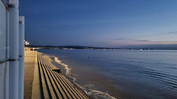 A waterfront promenade with a wooden walkway and a calm sea.