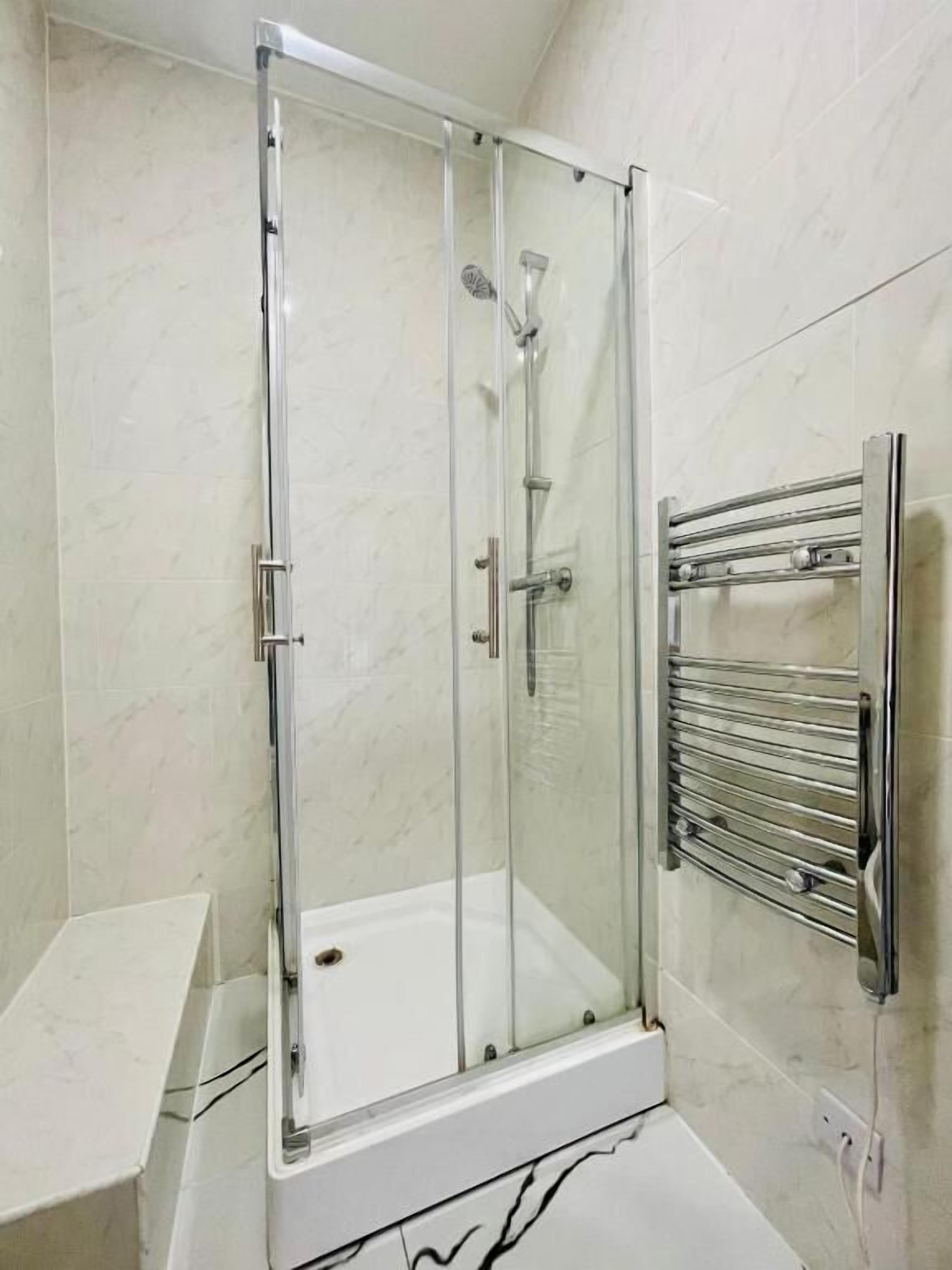 A glass-enclosed shower with a chrome frame, a white tiled wall, and a chrome towel rail.