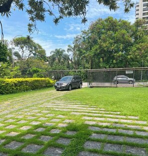 Ein gepflasterter Gartenbereich mit einem geparkten Auto in der Nähe eines Zauns, umgeben von üppigem Grün und Bäumen.