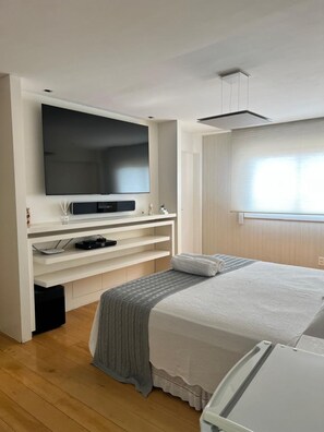 Ein modernes Schlafzimmer mit Flachbildfernseher, eingebauten Regalen, einem Bett mit grauer Decke und einem Fenster mit Jalousien.