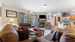 Sala de estar con sofás de cuero, una mesa de centro, chimenea, televisor y una cocina con armarios de madera.