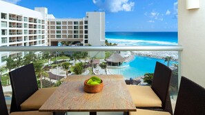 Ein Balkon mit Tisch und Stühlen, mit Blick auf einen Pool und Strand, im Hintergrund Hotelgebäude.
