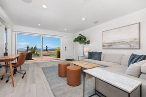 A modern living room with a sofa, coffee table, and a large window with a view of the outdoors. - Solana Luxe - New! Luxury Remodeled Oceanfront with AC (Solana Beach)