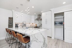 A modern kitchen with a marble island, bar stools, and a built-in oven. - Solana Luxe - New! Luxury Remodeled Oceanfront with AC (Solana Beach)