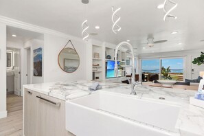 A modern kitchen with a large island, a built-in sink, and a dining area with a view. - Solana Luxe - New! Luxury Remodeled Oceanfront with AC (Solana Beach)