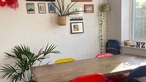 Un coin repas avec une table en bois, des chaises rouges et bleues, une décoration représentant une tête de lion rouge, une plante fixée au mur et un tableau encadré.