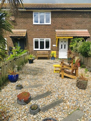 A brick house with a tiled roof, a wooden bench, and a yellow table in the garden. - Two minutes walk from beach. Located on quiet pathway. Dogs welcome. (Camber)