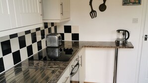 Une cuisine avec des meubles blancs, un pare-feu à carreaux, un grille-pain, une machine à café et un plancher en bois.