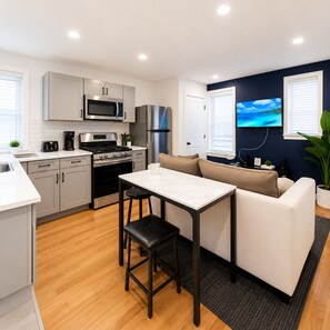 A compact kitchen with modern appliances, a dining area with a table and stools, and a living space with a sofa and a TV. - Enjoy a relaxed stay in this well-kept unit offering free parking, a stocked kitchen, and an in-suite washer/dryer. Great for work or leisure trips. (Rochester)