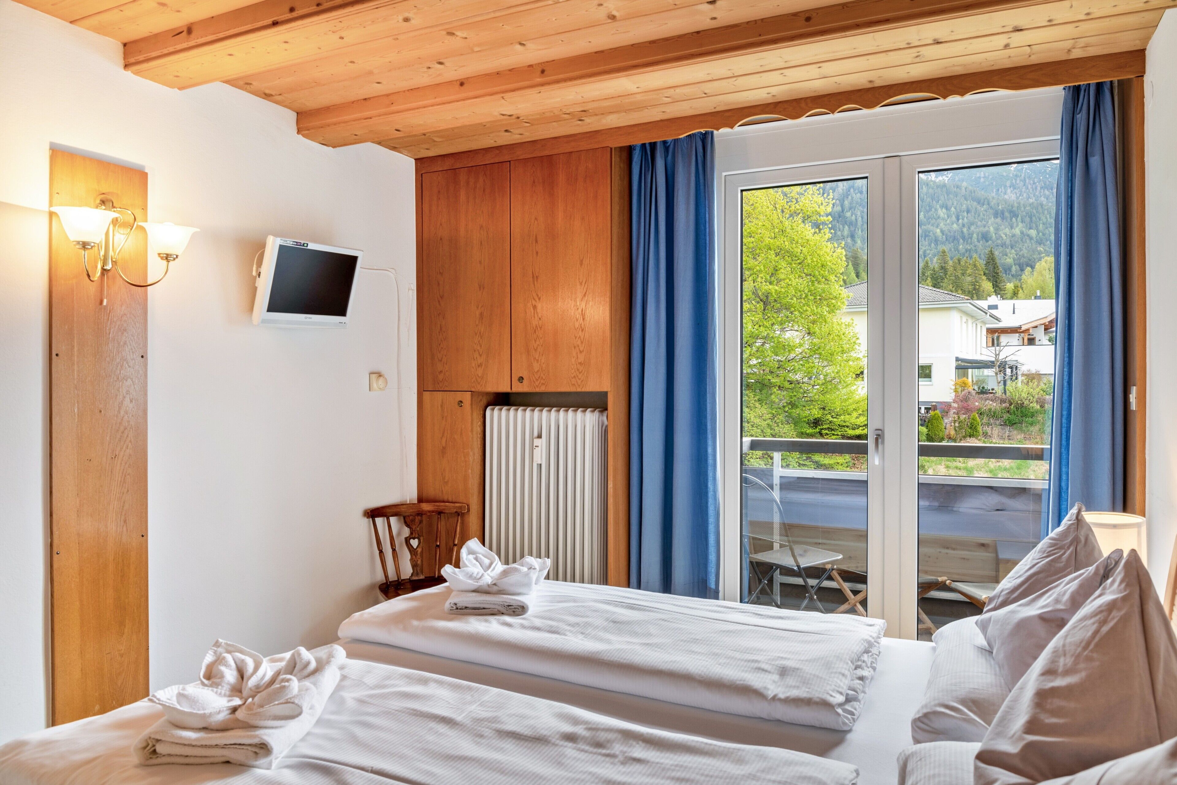 Une chambre d’hôtel avec un lit, une télévision, un plafond en bois, une fenêtre avec des rideaux et une vue sur l’extérieur.