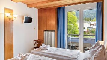 Une chambre d’hôtel avec un lit, une télévision, un plafond en bois, une fenêtre avec des rideaux et une vue sur l’extérieur.