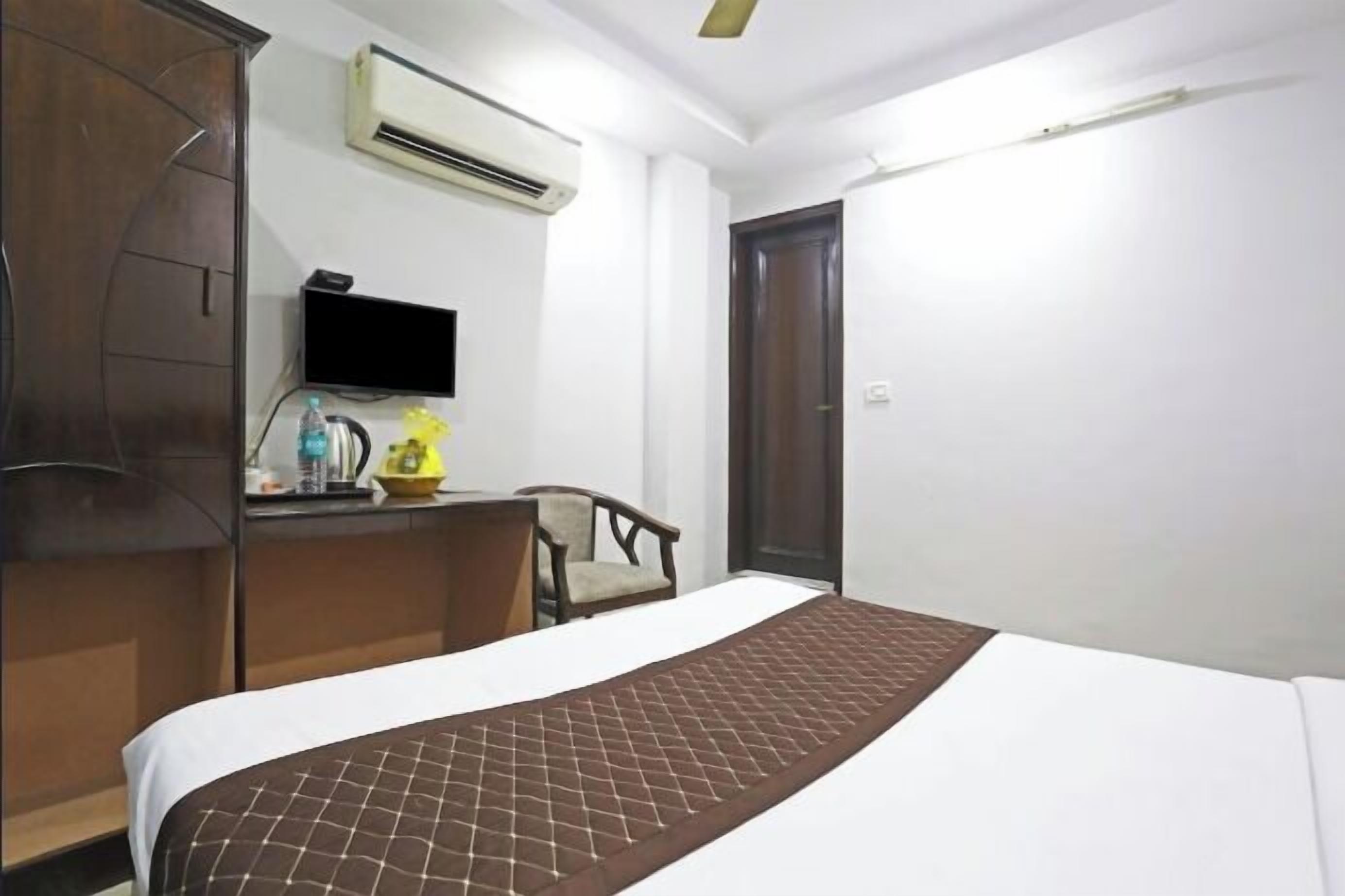A hotel room with a bed, a desk with a flat-screen TV, an air conditioner, and a wardrobe.