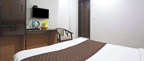 Una habitación de hotel con cama, escritorio con televisor de pantalla plana, aire acondicionado y armario.
