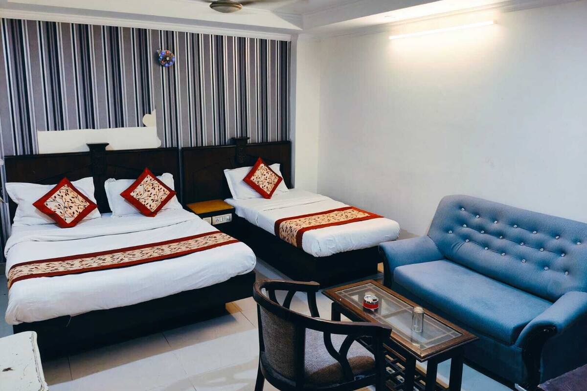 Habitación de hotel con dos camas, un sofá azul, una mesita y un ventilador de techo.