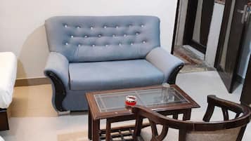 A living room with a blue sofa, a glass coffee table, and a wooden chair.