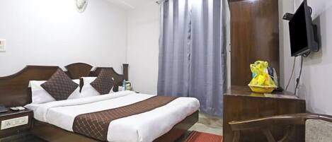 A hotel room with a bed, a desk, a chair, a television, and a wardrobe.