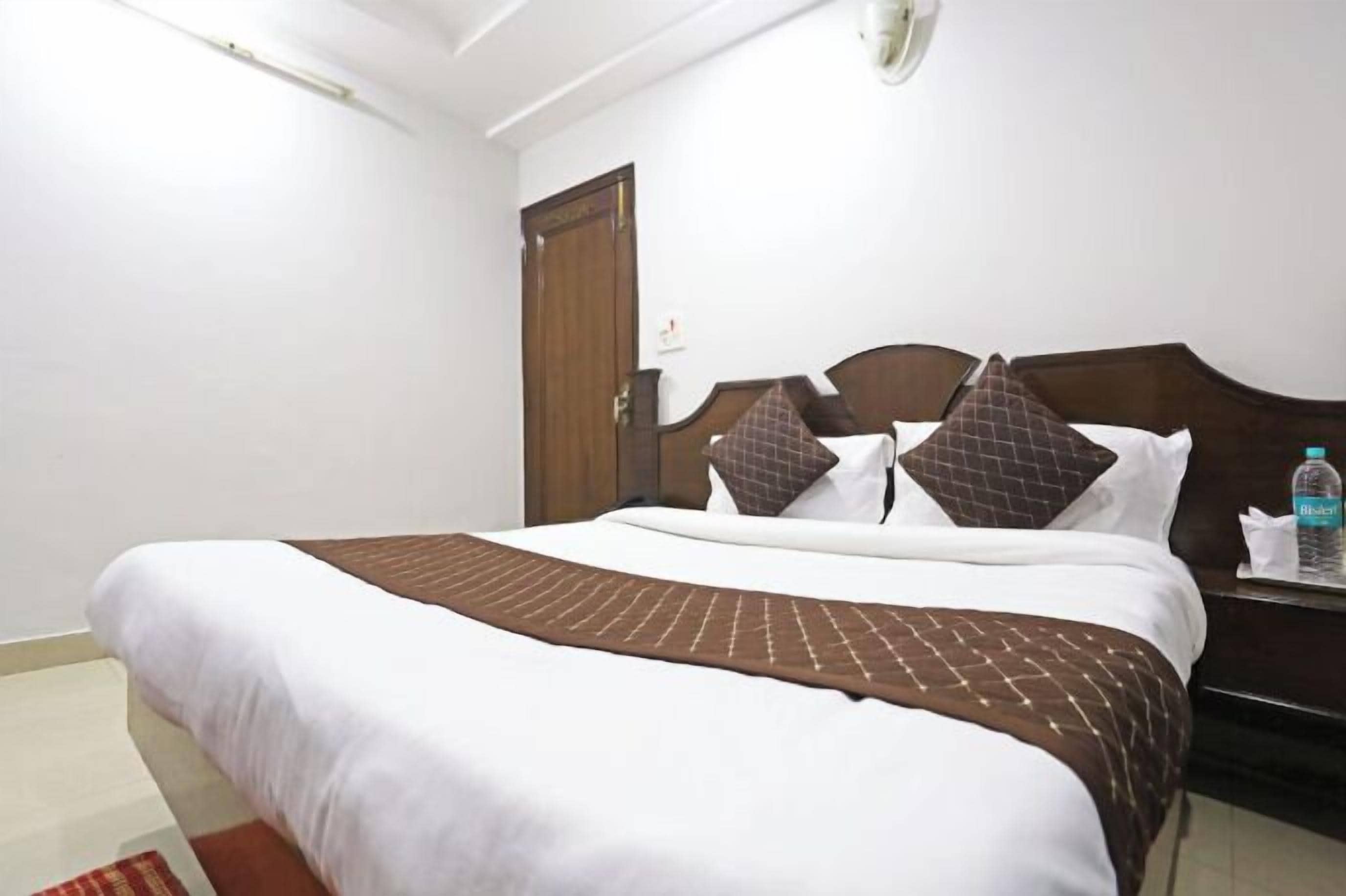 A hotel room with a bed, a wooden headboard, a nightstand, and a door.
