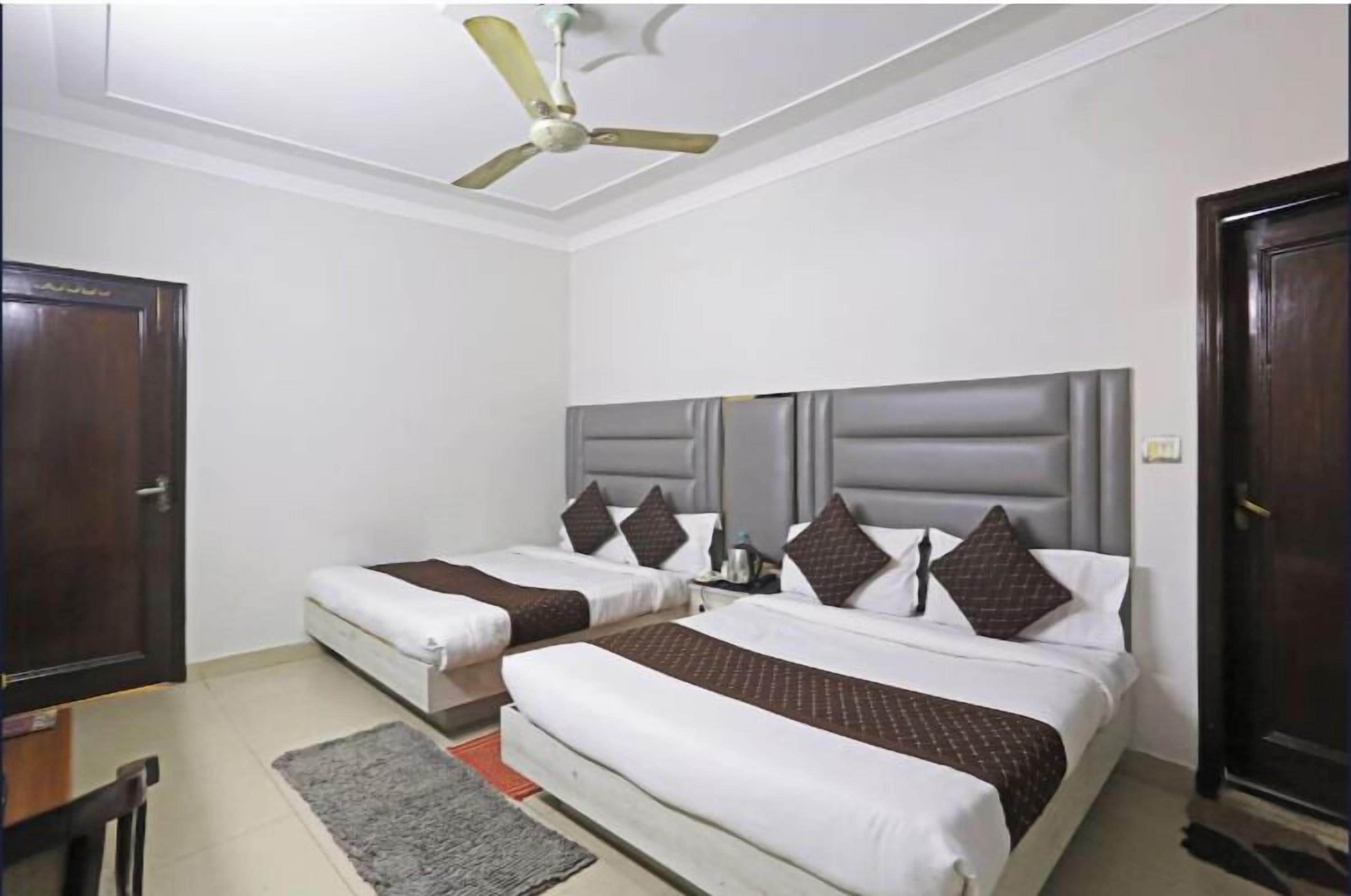 A hotel room with two beds, a ceiling fan, a desk, and a door.