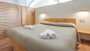 Une chambre moderne avec une tête de lit en bois, un lit recouvert d’une couverture beige à texture et deux lampes fixées au mur.