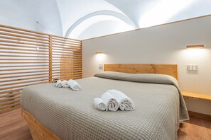 A modern bedroom with a wooden headboard, a bed with a textured beige blanket, and two wall-mounted lights. - Ragione - City Center Apt by Wonderful Italy (Catania)