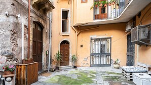 Une cour dallée de pierres, avec des portes en bois, des plantes en pot et du mobilier d’extérieur.