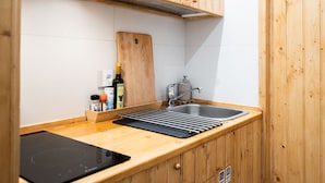 Cocina compacta con armarios de madera, un lavamanos, tabla de cortar y estufa integrada.