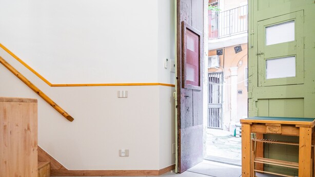 Une pièce avec un escalier en bois, une porte verte et une petite table en bois.
