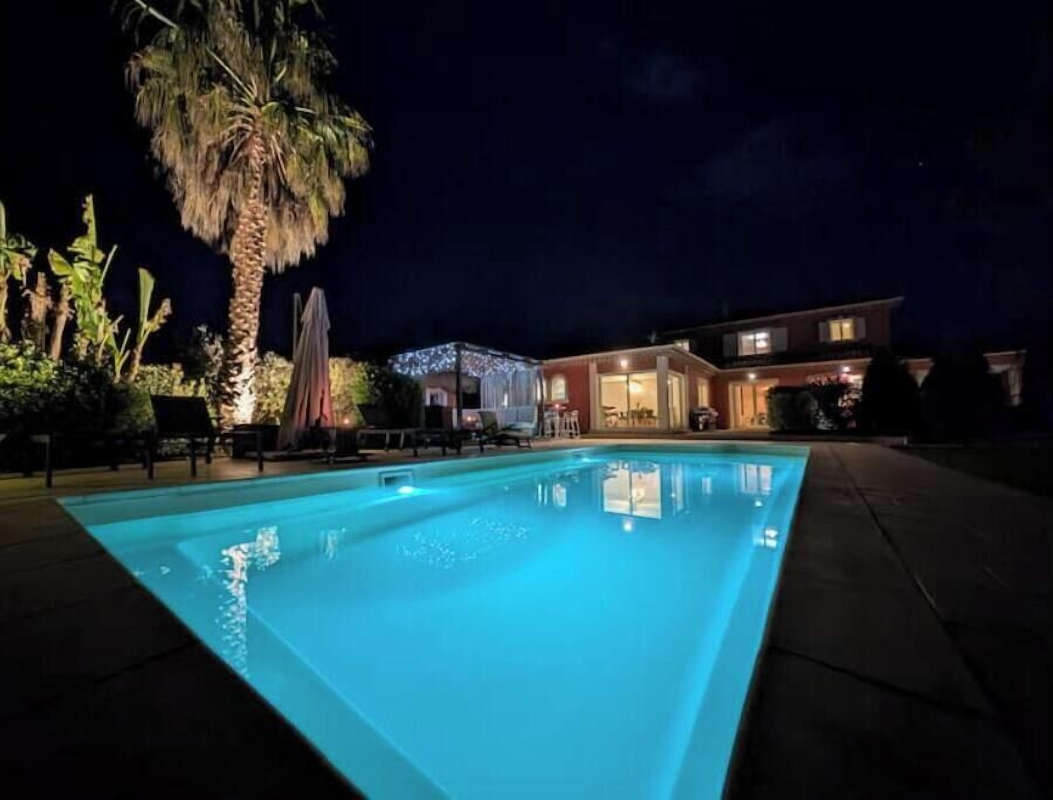 A swimming pool at night with a house in the background.