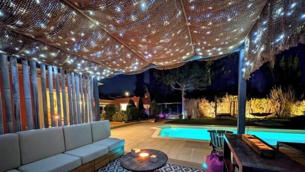 An outdoor patio area with a pool, a white sofa, a round table with a candle, and string lights. - Studio Le Mas de Provence with pool and jacuzzi - charm and relaxation (Le Cannet-des-Maures)