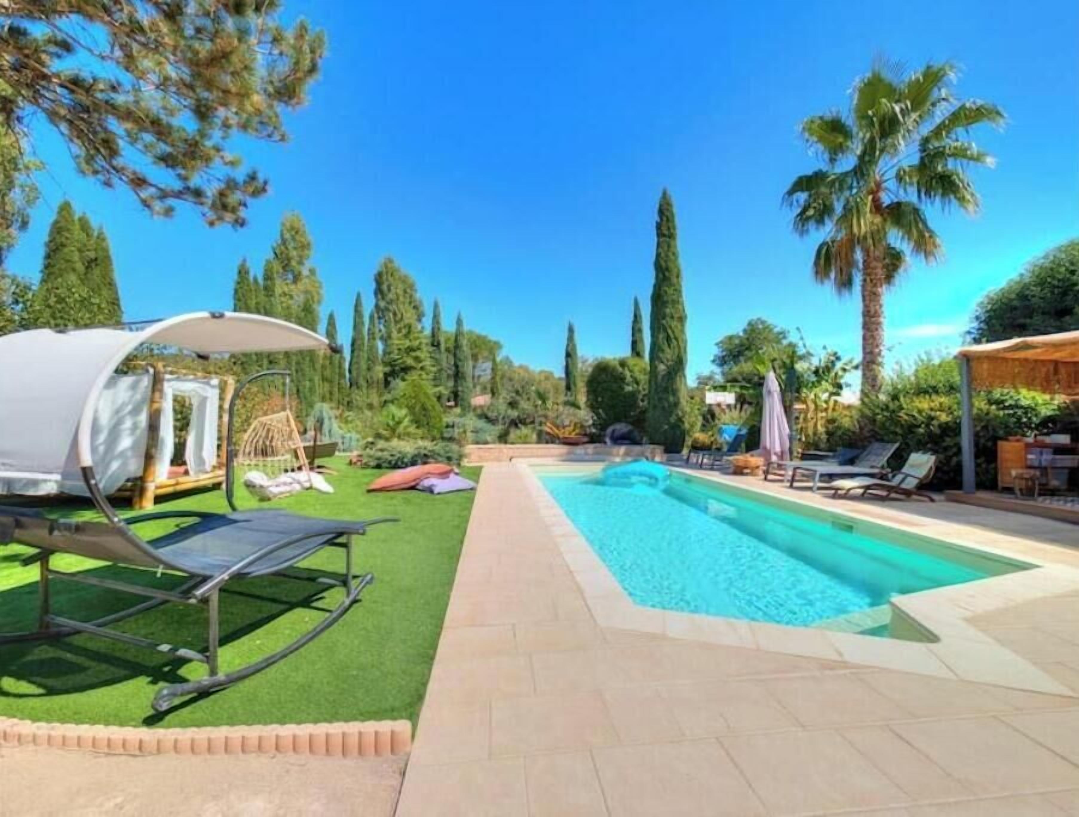 A swimming pool with lounge chairs, a tent, and palm trees.