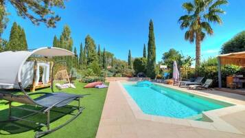 A swimming pool with lounge chairs, a tent, and palm trees.