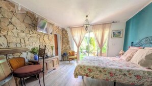 A room with a bed, a chair, a table, a stone wall, and a view of the outdoors. - Studio Le Mas de Provence with pool and jacuzzi - charm and relaxation (Le Cannet-des-Maures)