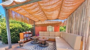 A covered outdoor seating area with a sofa, a table, and a bookshelf. - Studio Le Mas de Provence with pool and jacuzzi - charm and relaxation (Le Cannet-des-Maures)