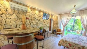 A room with a stone wall, a round wooden bar, a bed with floral bedding, and a TV mounted on the wall. - Studio Le Mas de Provence with pool and jacuzzi - charm and relaxation (Le Cannet-des-Maures)