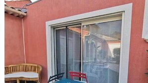Une terrasse avec une table et des chaises bleues, un banc en bois et une porte-fenêtre coulissante.
