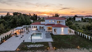 Una moderna casa a due piani con piscina, immersa in un giardino curato e con vista sul tramonto.