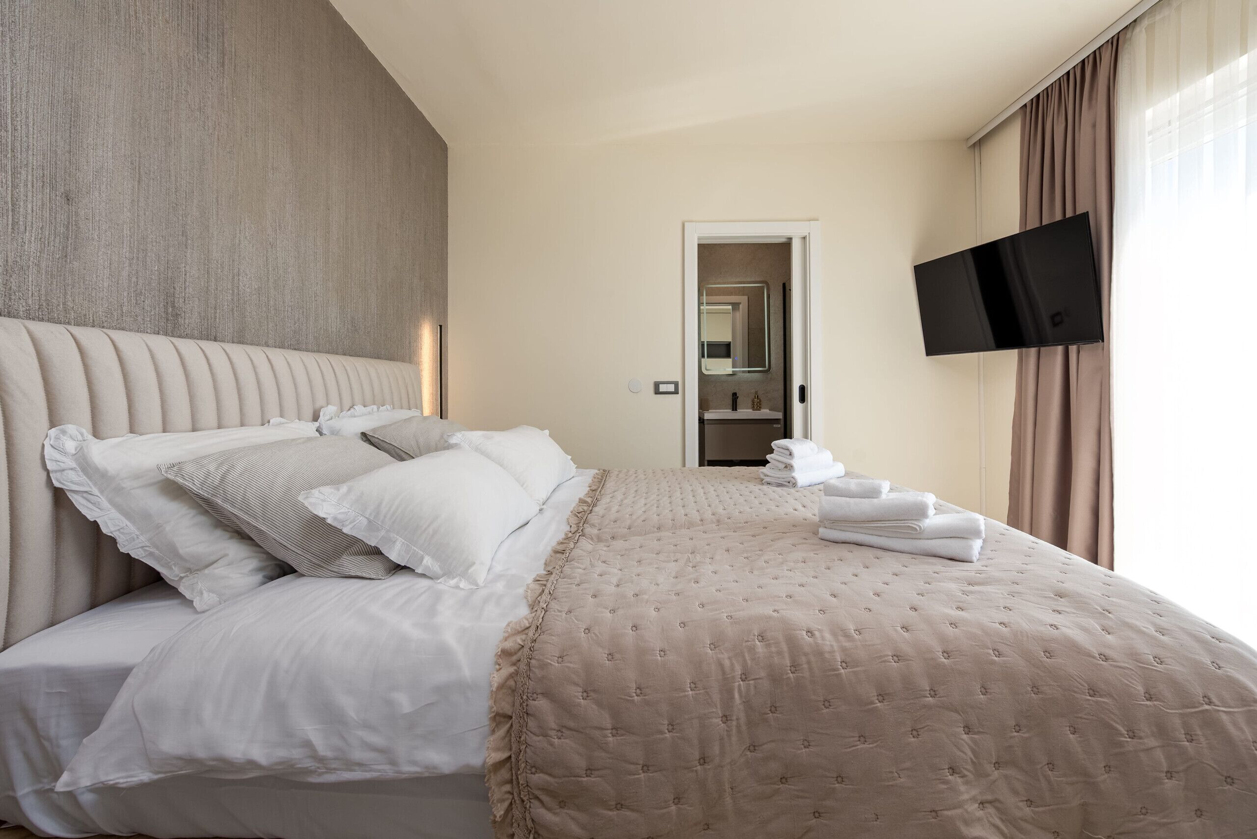 Ein Hotelzimmer mit einem großen Bett, einem wandmontierten Flachbildfernseher und einer Tür zu einem Badezimmer.