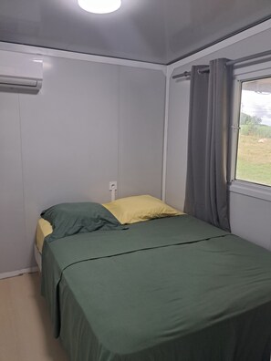 Ein Einzelbett mit Bettwäsche in Grün und Gelb in einem Zimmer mit Fenster und Vorhängen.