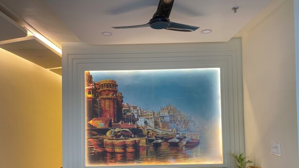 A modern living room with a large wall-mounted artwork of a cityscape, a ceiling fan, and a blue sofa. - Awesome 9-bedroom hotel with AC in vibrant Varanasi (Varanasi)