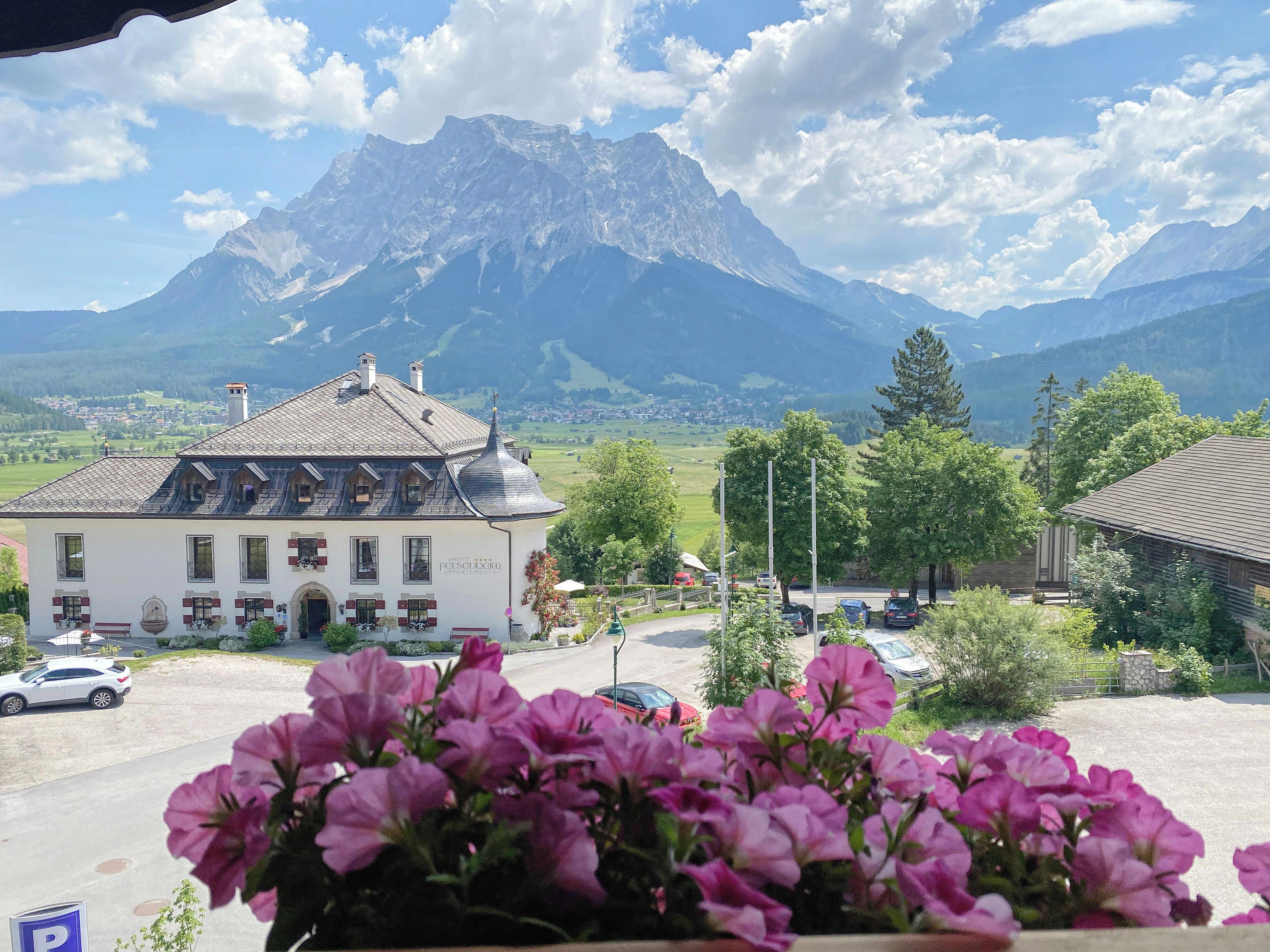 A building with a traditional architectural style, a parking area, and a mountain range in the background.