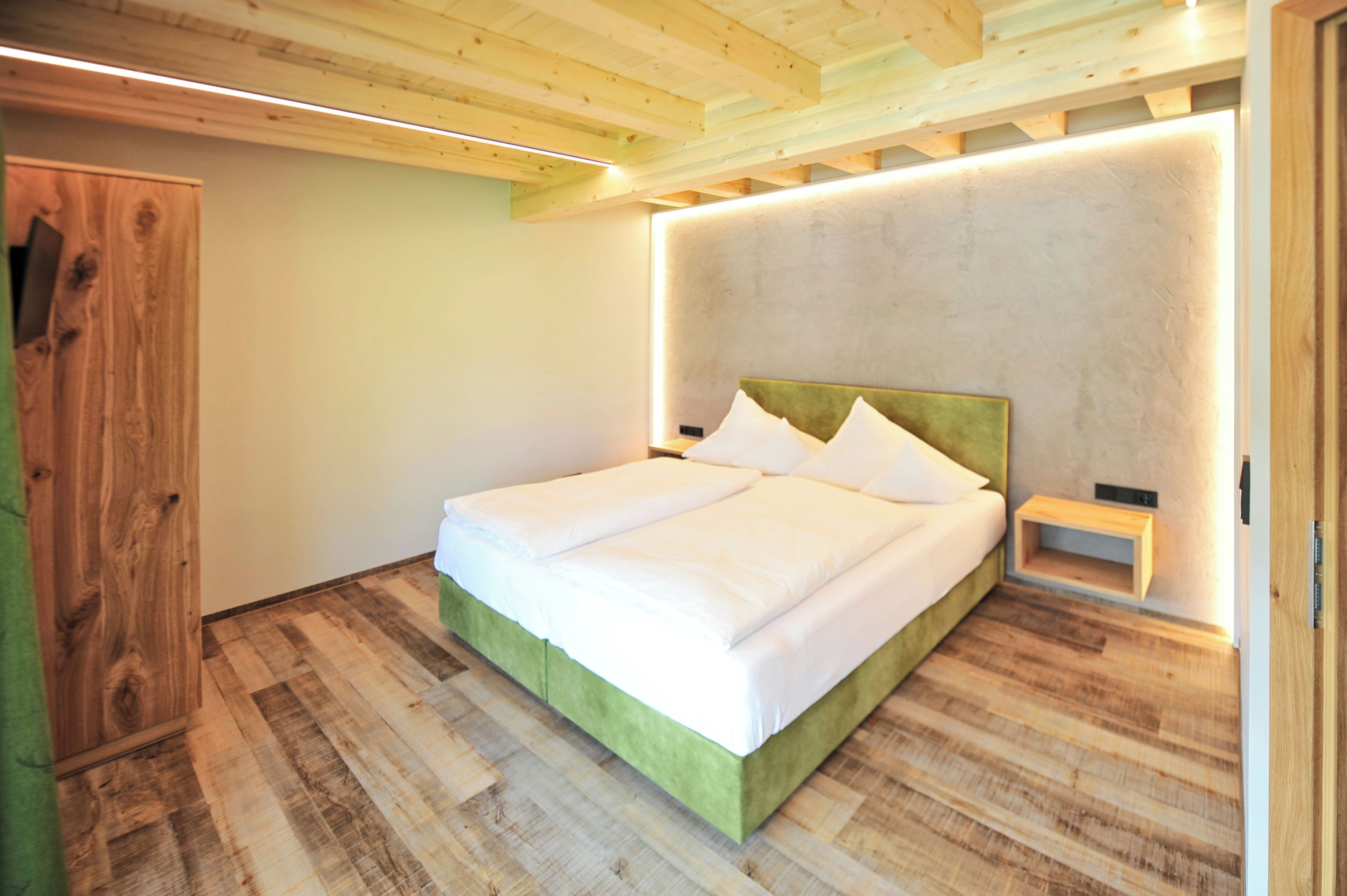 Une chambre avec un plancher en bois, un cadre de lit vert, du linge de lit blanc et une table de chevet.
