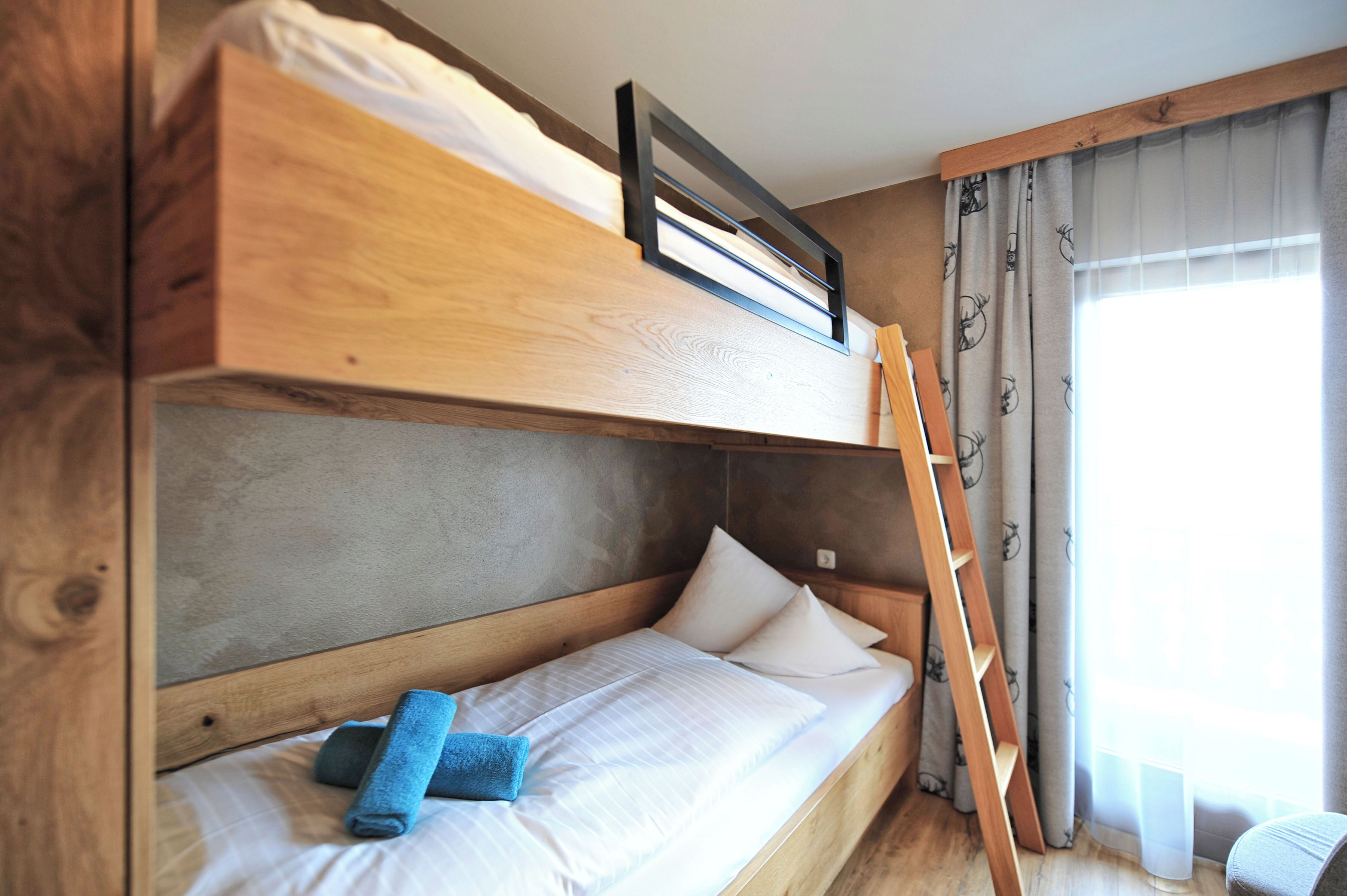 A bunk bed with a ladder, a window with curtains, and a small chair.