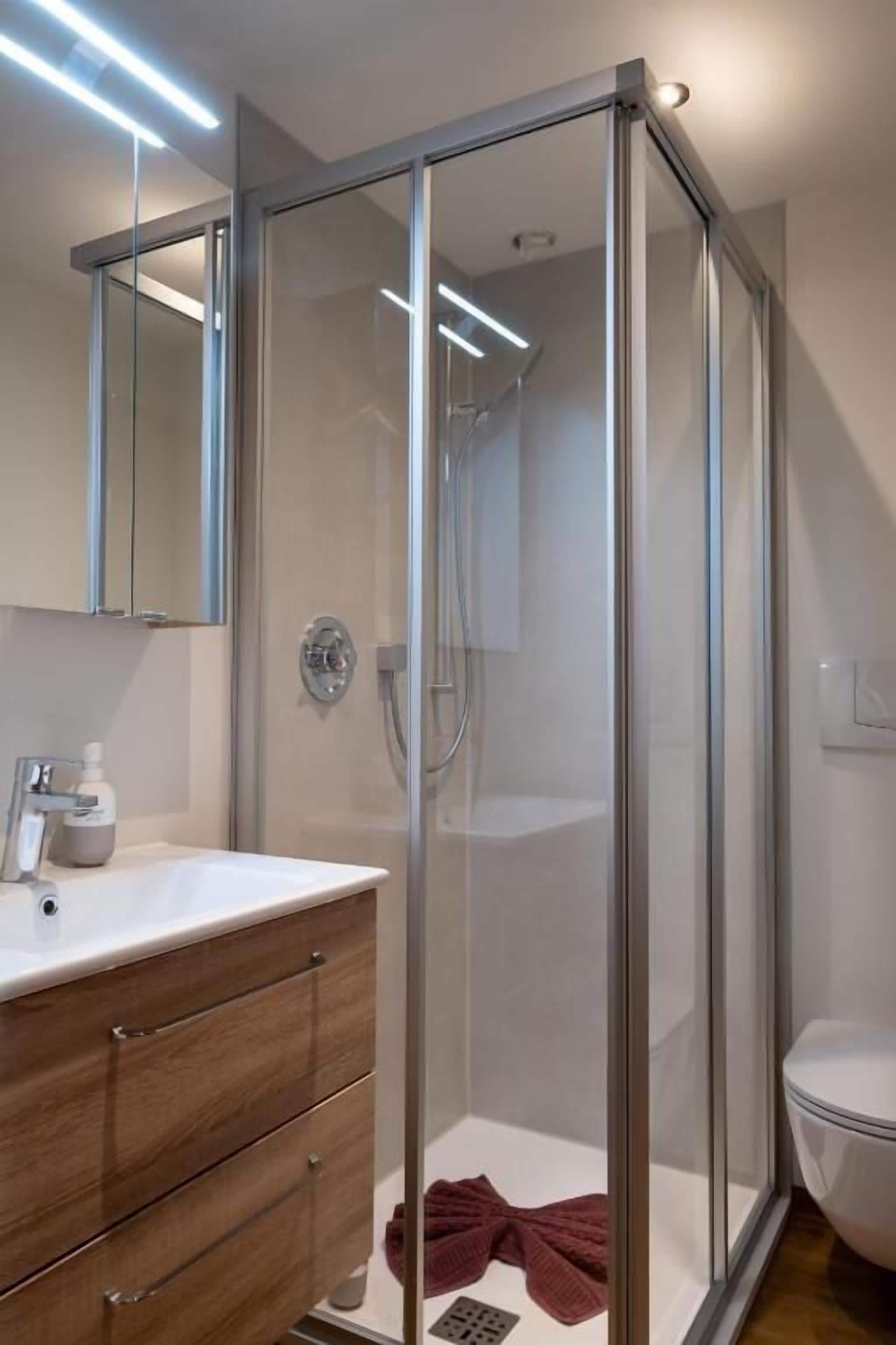 Un baño moderno con cabina de ducha de vidrio, lavabo blanco y tocador de madera.