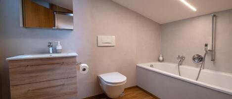 A modern bathroom with a wooden vanity, a toilet, a bathtub, and a mirror.