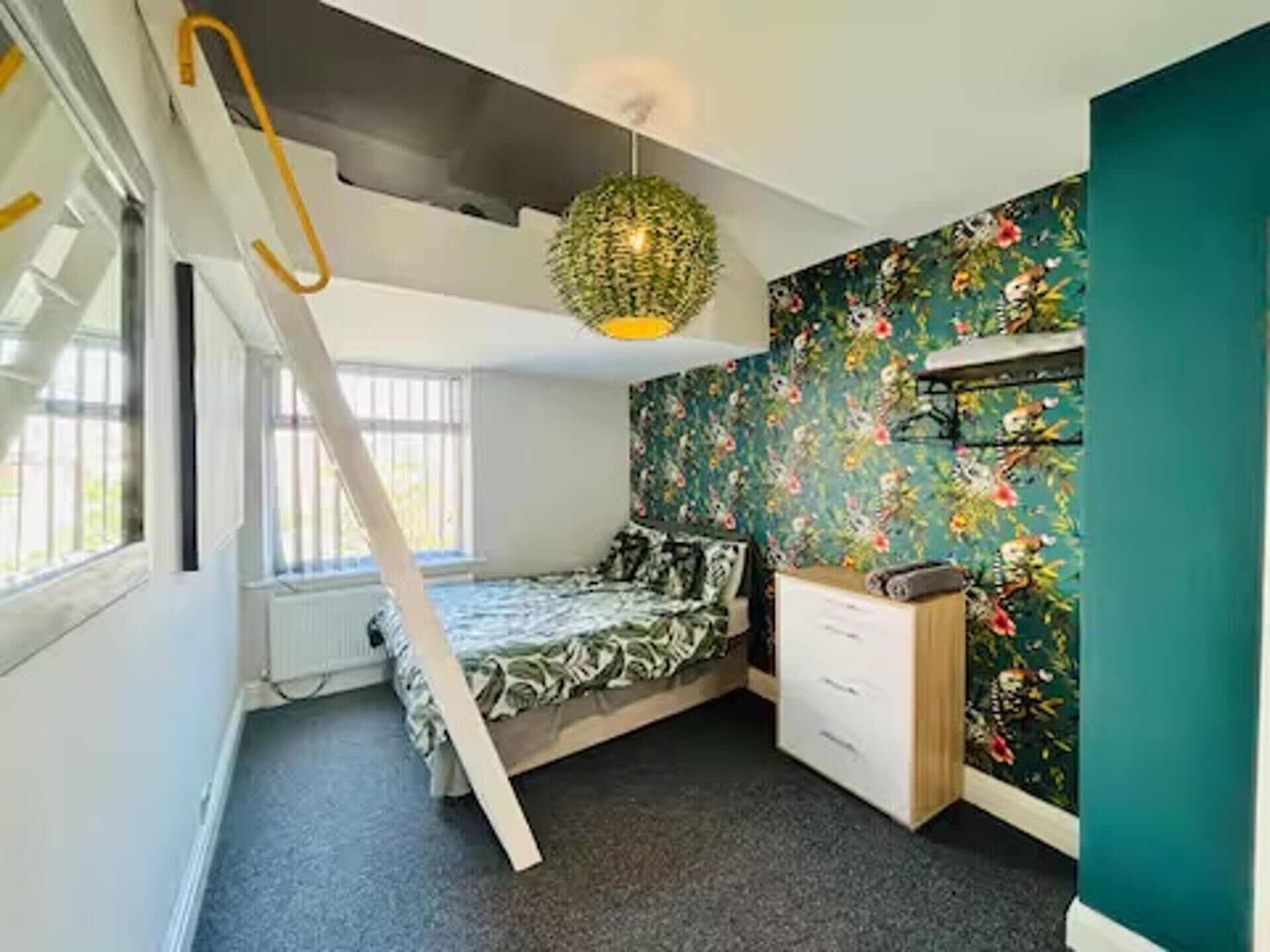 Een slaapkamer met een stapelbed, een dressoir, een hanglamp en een raam met jaloezieën.