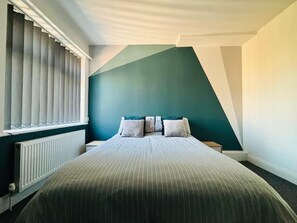 A bedroom with a bed, a window with blinds, a radiator, and a green wall. - Blackpool Bliss Spacious 4 Bedroom House (Blackpool)