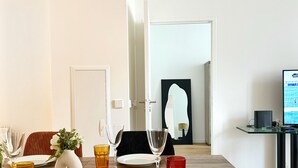 Un comedor moderno con una mesa de madera dispuesta para cuatro personas, un jarrón con flores y un vaso rojo.