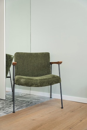A chair with a high backrest and wooden armrests, positioned in a room with a tiled floor and a large mirror on the wall. - Historic Center Studio | City Views on Ceuta (Porto)