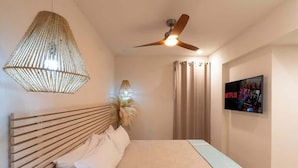 Quarto com cama, ventilador de teto, televisão na parede e luminária pendente.