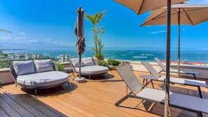 Um terraço com espreguiçadeiras e um sofá, com vista para a costa.
